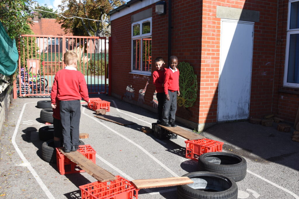 Three school children in red and grey uniform, playing in the playground on apparatus.