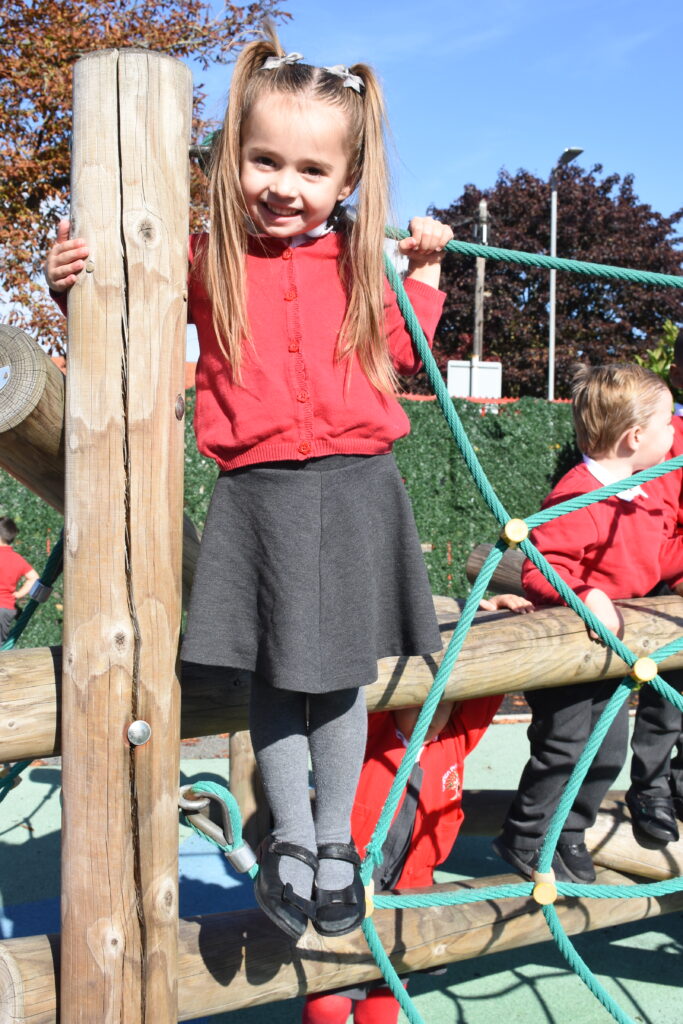 Young girl on playground apparatus, wearing red and grey school uniform, looking at the camera