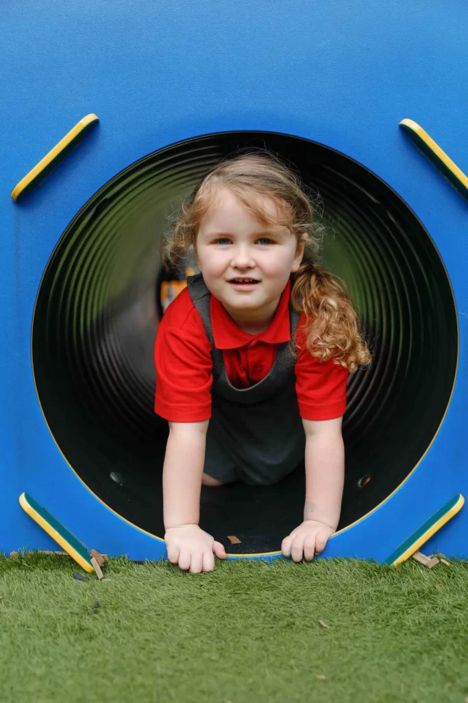 Young school girl in a red and grey uniform, at the bottom of a slide, looking at the camera.