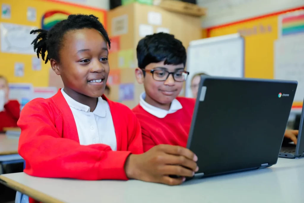 Two school children wearing red uniform, looking at a laptop together